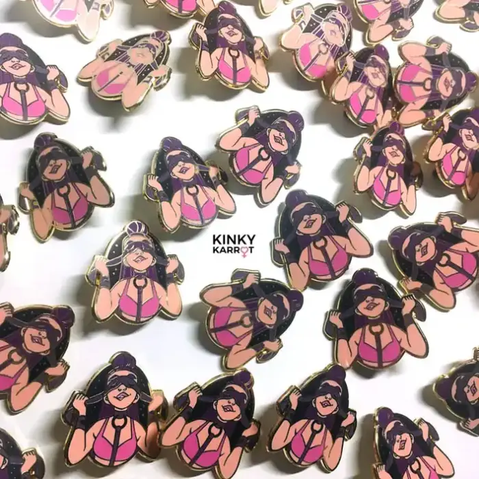 blindfold enamel pin with femme figure in pink harness smiling with mask