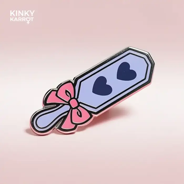 Heart version of Spanking Paddle Enamel Pin with pink bow and two navy hearts on a light purple blade.