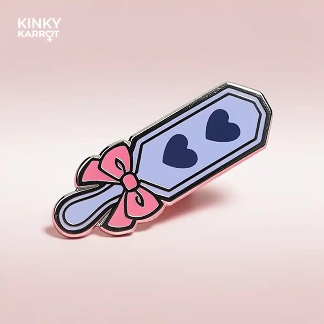 Heart version of Spanking Paddle Enamel Pin with pink bow and two navy hearts on a light purple blade.