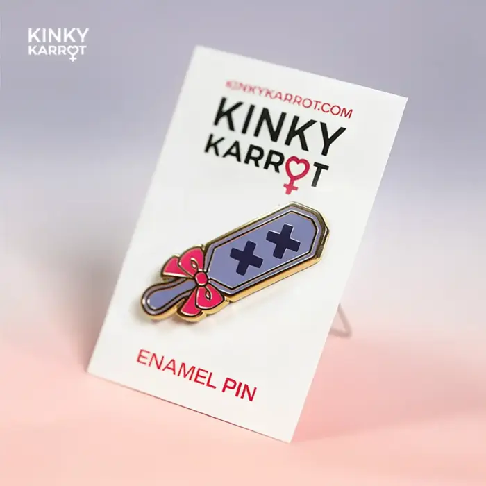 Spanking Paddle Enamel Pin attached to KINKY KARROT product card, angled for display.